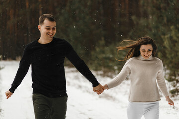 Wall Mural - Smiling couple in love walking in the winter forest holding each other hands. Love, relationship, winter holidays. Winter couple photo ideas