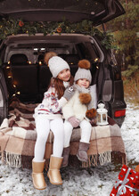 Two Teenage Girls Hug In The Trunk Of A Car Decorated With Christmas Decorations Around A Lot Of Gifts. Waiting For Christmas. Snowy Weather.