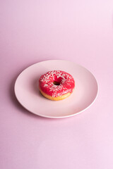 Pink red donut with white sprinkles on pink plate, sweet glazed dessert food on pink minimal background, angle view