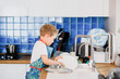 a boy in an apron washes dishes in the kitchen at home.