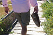 © Wavebreak Media - Midsection of senior caucasian holding shoes walking down steps to beach
