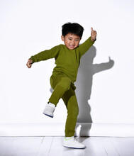 Fashion Portrait Of Cute Little Kid Boy In Stylish Green Tracksuit Dancing Break Against White Studio Wall. The Concept Of Sports And Healthy Activities For The Modern Child.