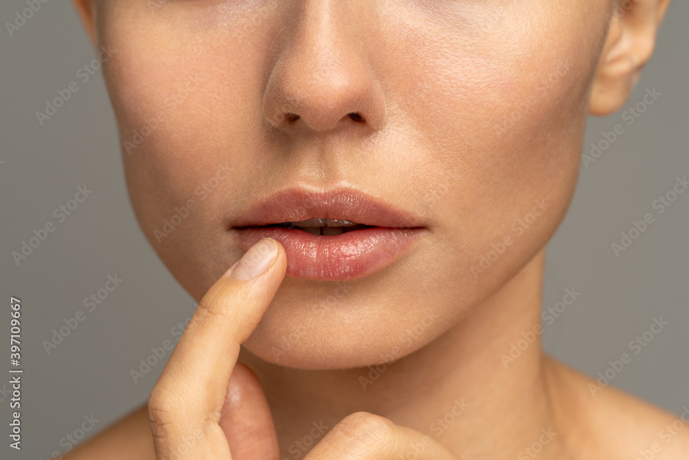 Close up of woman applying moisturizing nourishing balm to her lips with her finger to prevent dryness and chapping in the cold season. Lip protection.  - obrazy, fototapety, plakaty 