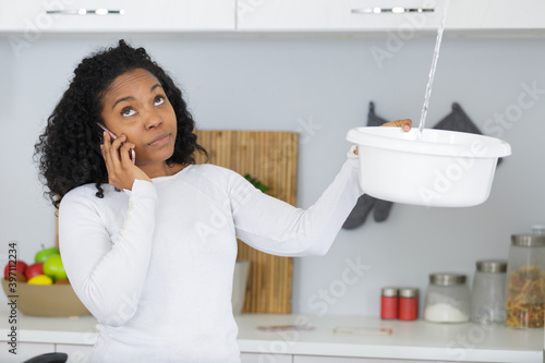 stressed woman calling plumber to fix water leaking from ceiling
