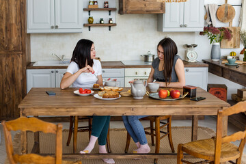 Two girls are drinking tea with cake and sweets at the table.