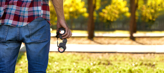 Man hands with a binoculars standing in the forest at the time the sun is about to set.