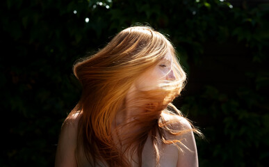 Sensual sexy portrait of young beautiful redheaded woman shakes her red hair outdoors in the sunlight with ivy background and green leaves, copy space