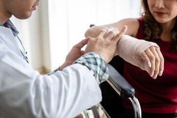 Close-up of man doctor with wrapping nurse bandages splint to the arm of a female patient wear arm splint with analogue pressure gauge for better healing In the room hospital background.