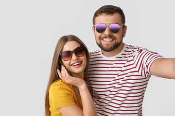 Wall Mural - Young couple with stylish sunglasses taking selfie on light background