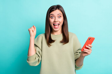 Poster - Photo portrait of woman celebrating with raised fist holding phone in one hand isolated on vivid teal colored background