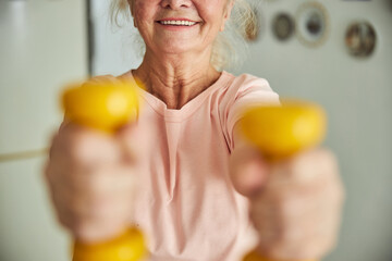 Cheerful elderly woman doing exercise with dumbbells at home