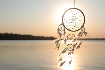 Beautiful handmade dream catcher near river at sunset. Space for text