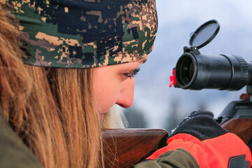 Wall Mural - A young hunter woman on hunt looks into the rifle a waiting for wild animal.