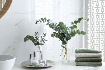 Fresh eucalyptus branches and cosmetic products on countertop in bathroom