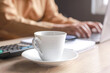 © Gatot - A cup of coffee on a desk office with blurry hand of businessman or worker typing on the laptop on the background