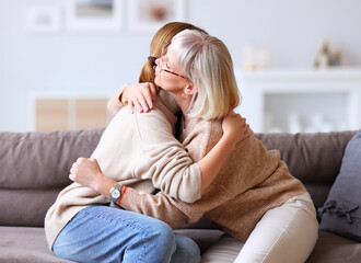 Supportive mother hugging daughter on couch.