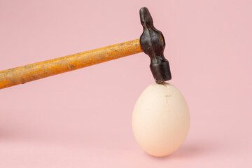 Hammer hit on an egg on pink background