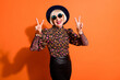 © deagreez - Photo of good mood happy smiling positive old woman show v-sign wear sunglasses black headwear isolated on orange color background