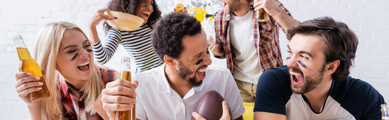 excited multiethnic friends with painted faces shouting while watching rugby championship, banner