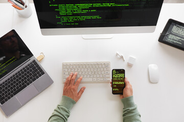Wall Mural - high angle view of programmer sitting at the table using computer laptop and mobile phone programmin