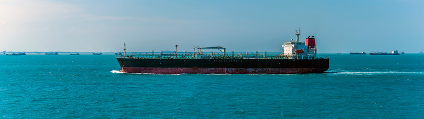 A lightly laden tanker sailing past moored vessels in the Singapore Straits in Asia in summertime