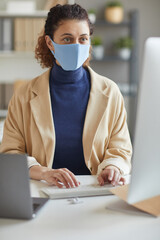 Wall Mural - young secretary in protective mask sitting at her workplace typing on computer keyboard working at o