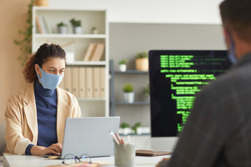 Wall Mural - developers in masks working at the table on computers with codes at office