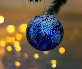 blue Christmas ball with frosty patterns hanging on a Christmas tree against a background of lights