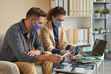 Wall Mural - two designers in protective masks working with professional photos in team during their meeting at o