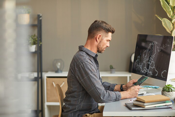 Wall Mural - serious graphic designer sitting at the table in front of computer and working at office