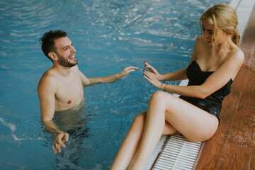 Wall Mural - Young couple relaxing on the poolside of interior swimming pool