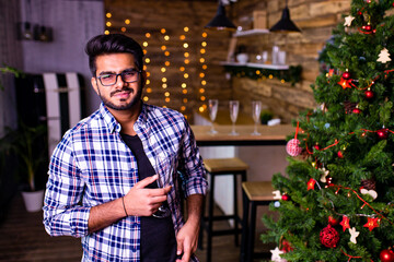 indian man drinking alcohol at studio shot spruce Christmas tree lights garland background