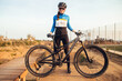 © Aitor Lamadrid/ADDICTIVE STOCK - Cheerful young female in sportswear and helmet standing on wooden platform with dusty mountain bike smiling and looking at camera