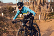 Sportswoman In Black Helmet And Blue Sportswear With Glasses Riding Mountain Bike On Training Track