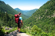 © Galdric Penarroja/ADDICTIVE STOCK - Back view of unrecognizable male hiker with backpack and trekking stick standing on grassy hilltop and admiring spectacular scenery of mountain ridge in summer day