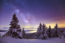 Glowing Northern Lights And Milky Way In Night Sky Over Mountainous Terrain With Coniferous Trees Covered With Snow In Wintertime