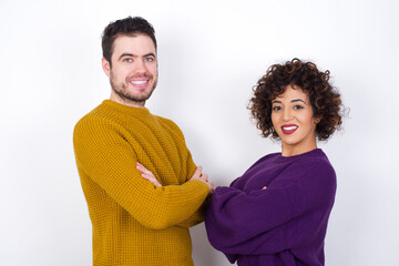 Wall Mural - Image of cheerful Young couple wearing knitted sweater standing against white wall with arms crossed. Looking and smiling at the camera. Confidence concept.