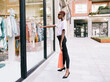 © Luis Manuel Munoz/ADDICTIVE STOCK - Full body side view of young slim African American female shopper in stylish outfit with shopping bag in hand standing near window of modern clothing store and looking at new collection