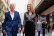 © Si And Si/ADDICTIVE STOCK - Low angle of serious determined senior businessman in elegant suit walking with smiling elegant female partner on urban street