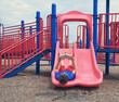 © Angela Waye/Stocksy - Boy Reading Outside on Red Slide Playground