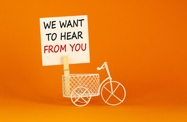 Wall Mural - Wooden clothespin with white sheet of paper. Text 'we want to hear from you'. Miniature bicycle model. Beautiful orange background. Business and support concept, copy space.