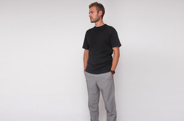 young stylish guy in black t-shirt and gray pants is standing straight on the white wall background. medical concept. free space on left side, mockup