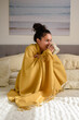 © JGI/Jamie Grill/Blend Images - Hispanic woman sitting on bed wrapped in blanket drinking coffee