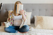 © JGI/Jamie Grill/Blend Images - Caucasian expectant mother sitting on bed reading book and drinking coffee