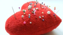 Pin Cushion In The Form Of A Soft Red Heart In Which Many Pins And Needles For Embroidery And Sewing Are Stuck In A Sewing Workshop Or Atelier.