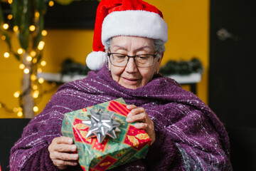 Wall Mural - latin elderly woman with gift expressing happiness at Christmas in home in Mexico city