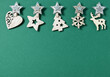 Christmas minimal flat lay composition. Border made of wooden Xmas decorations in shape of stars, xmas tree, snowflake and deer on green background. New Year, winter holidays. Top view, copy space.
