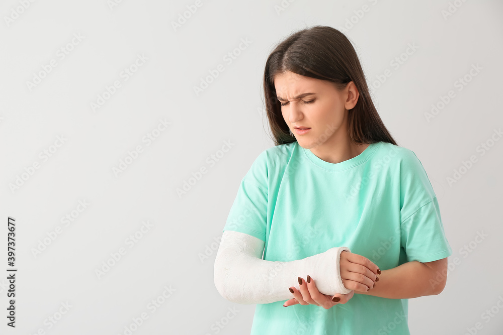 Young woman with broken arm on light background