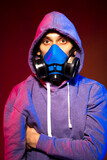 Fototapeta  - Portrait of an anonymous man, hacker wearing neon mask over dark background. Selective focus of bi-racial cyberpunk player holding guns near neon lighting