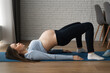 Beautiful pregnant woman doing exercises at home. Lies on his back and lifts up.